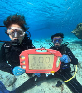 座間味のケラマブルーの海で100本記念のスレートを持つご夫婦ダイバー。透明度30mの美しい海で迎えた記念ダイビング。